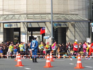 台灣跑者拿著國旗經過地鐵豐洲站前，距離終點的國際展示場已不遠