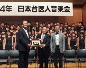 高醫校長劉景寬（左）和日本台醫人音樂會會長宮田功健（中）互贈紀念品（圖右為南杏合唱團指揮翁文國）