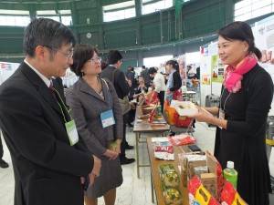 台北駐日経済文化代表処那覇分処の蘇啓誠処長（左１）と台湾貿易センター福岡事務所の林淑恵所長（左２）に商品の説明をする摩士國際顧問有限公司の劉如華CEO（右）